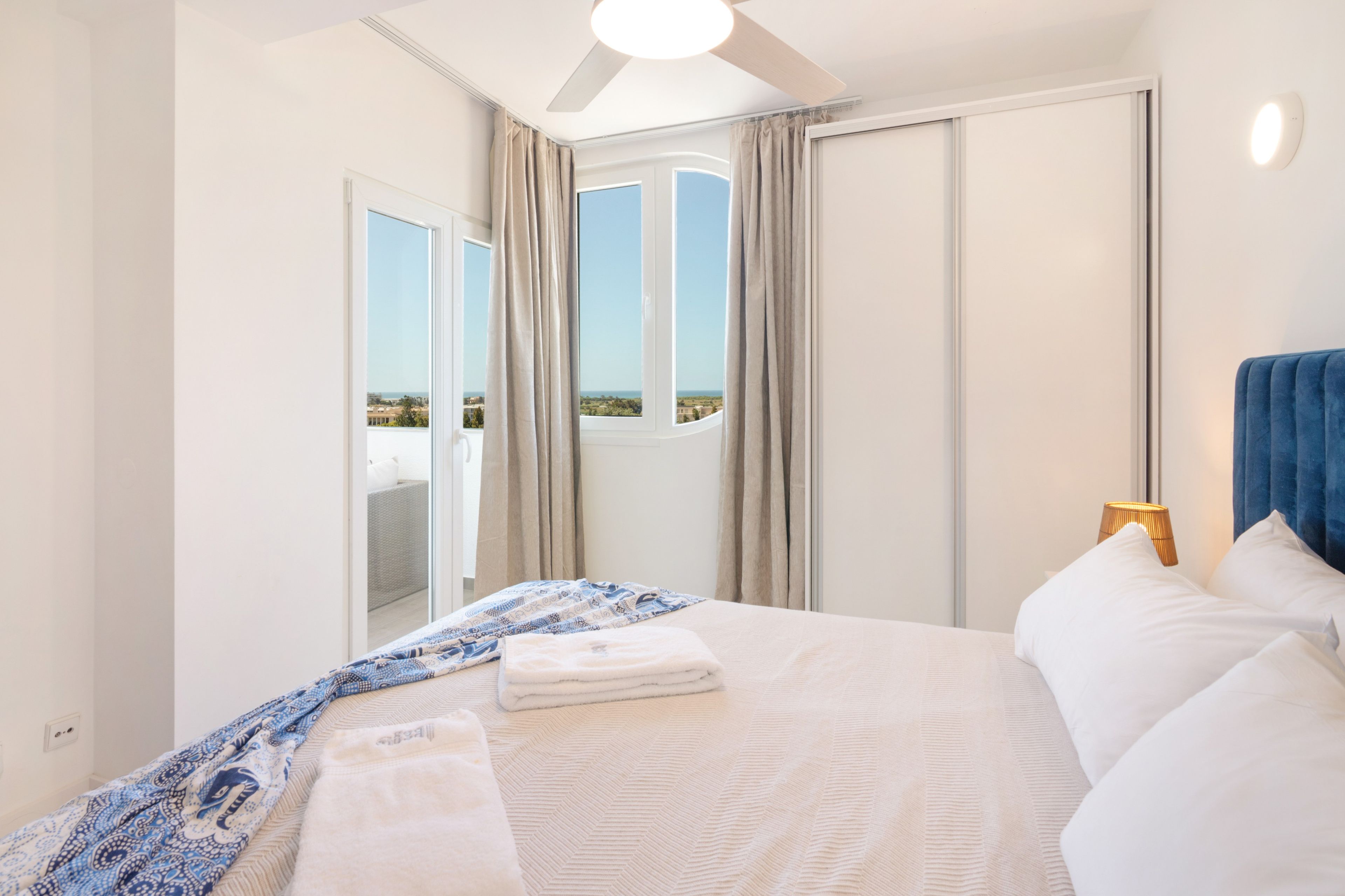 Une chambre d’hôtel avec un lit, une fenêtre avec des rideaux, un ventilateur de plafond et une vue sur l’extérieur.