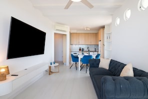A modern living room with a flat-screen TV, a sofa, and a dining area with blue chairs.