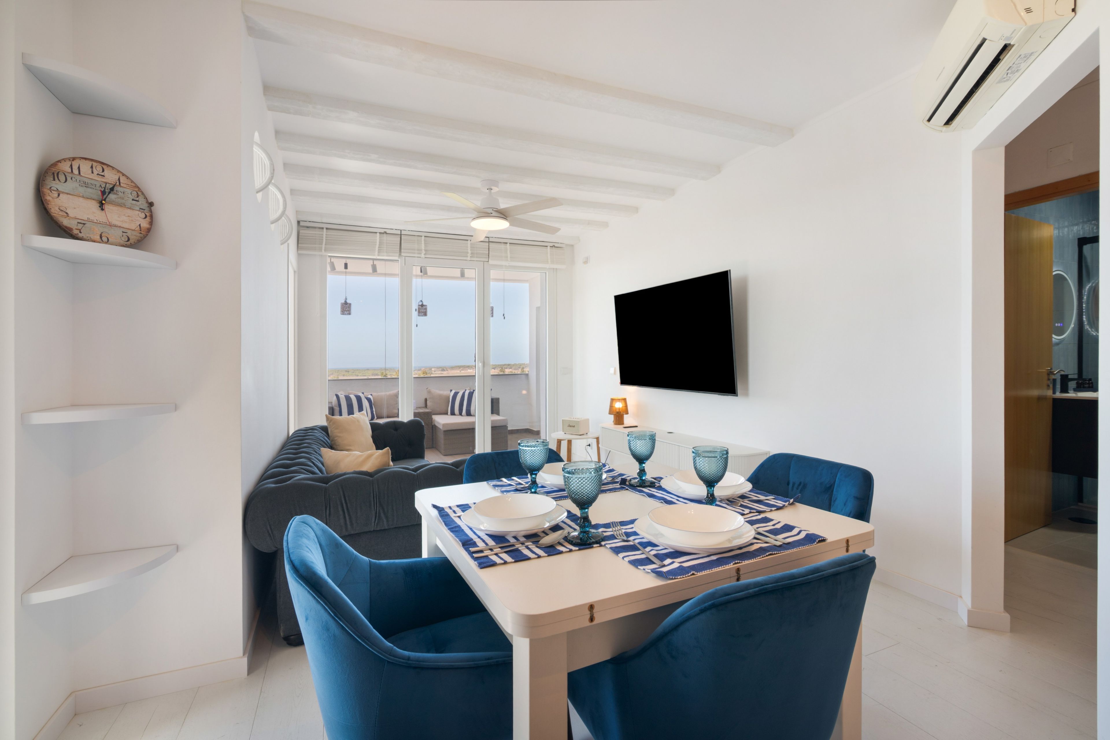Un coin repas avec une table dressée pour quatre personnes, un canapé et un téléviseur fixé au mur.