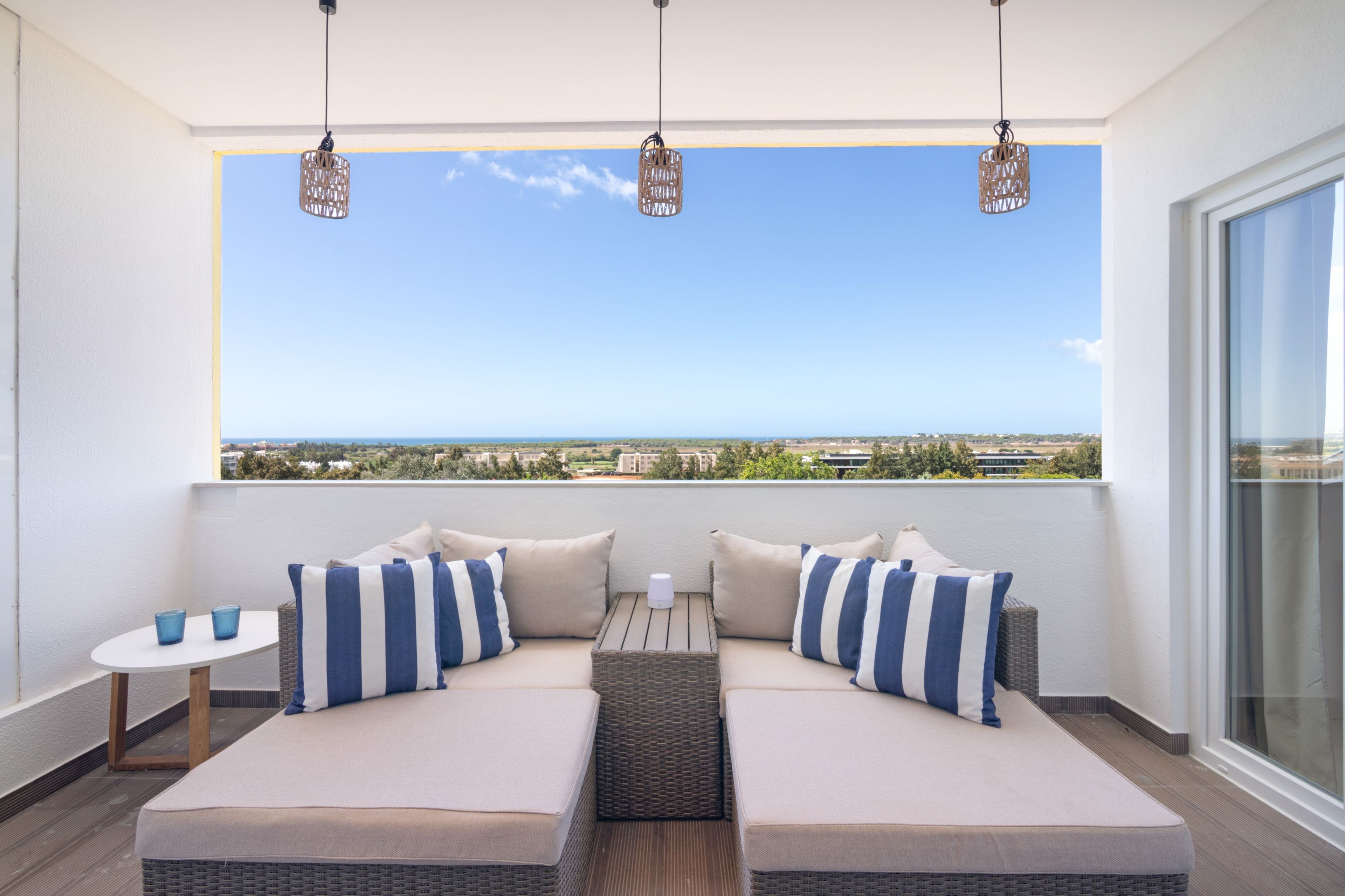 Un balcon doté de deux coins salon avec des sièges rembourrés, d’une petite table et de luminaires suspendus.