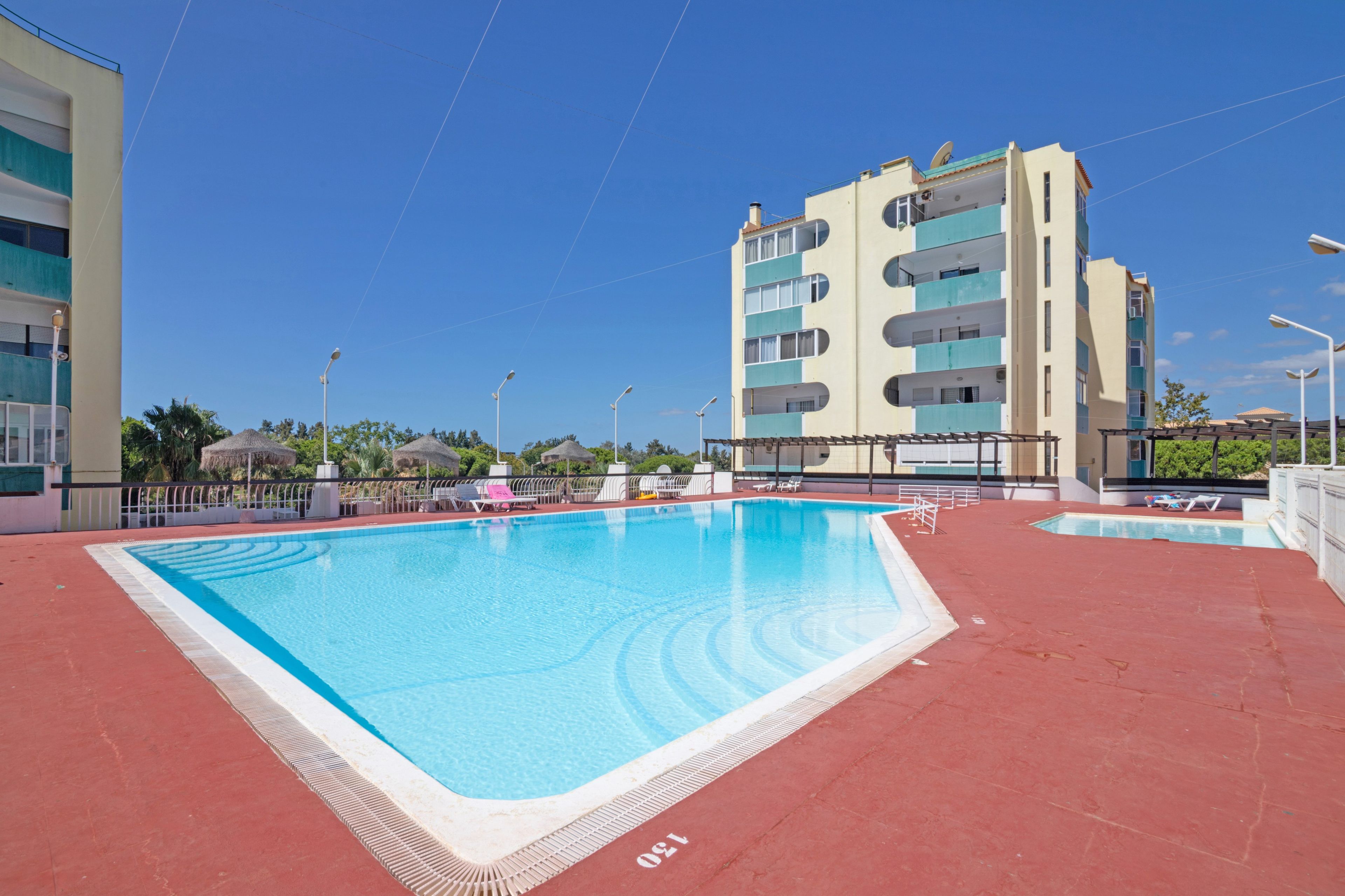 A swimming pool with a red deck, surrounded by a building with multiple balconies.