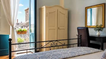 A bedroom with a bed, a desk, a chair, a wardrobe, and a view of the city through a window.