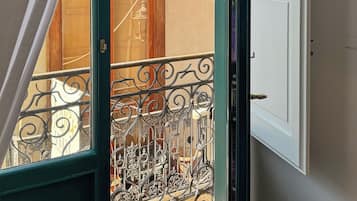 An open door with a view of a balcony, a metal railing, and a building in the background.