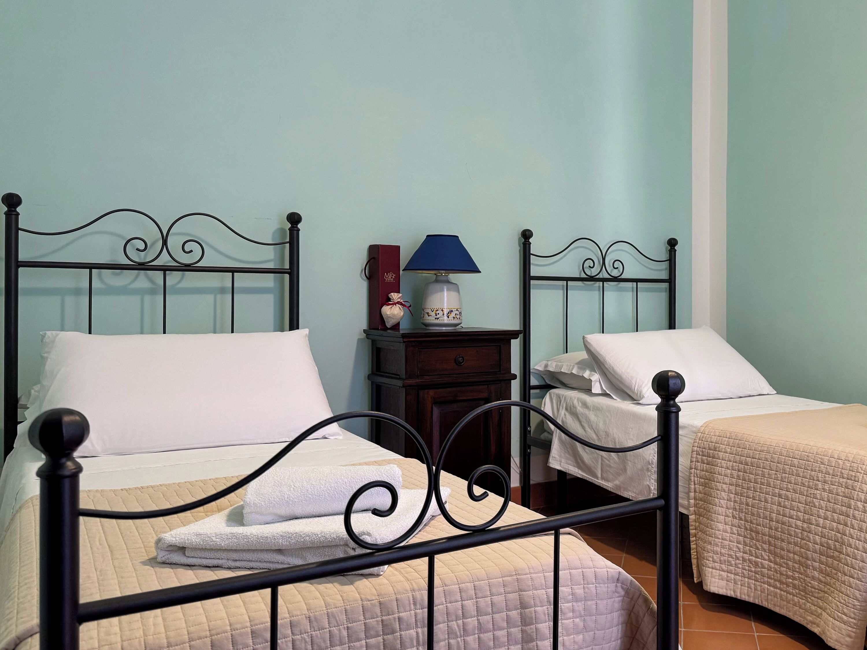 Una habitación con dos camas, cada una con una almohada blanca y un edredón acolchado color beige. Hay una mesita de noche con una lámpara y un pequeño objeto decorativo entre las camas.