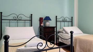 Una habitación con dos camas, cada una con una almohada blanca y un edredón acolchado color beige. Hay una mesita de noche con una lámpara y un pequeño objeto decorativo entre las camas.