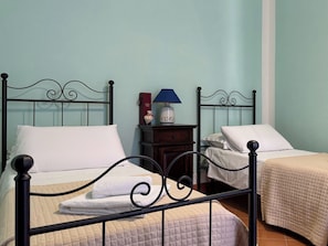 Una habitación con dos camas, cada una con una almohada blanca y un edredón acolchado color beige. Hay una mesita de noche con una lámpara y un pequeño objeto decorativo entre las camas.