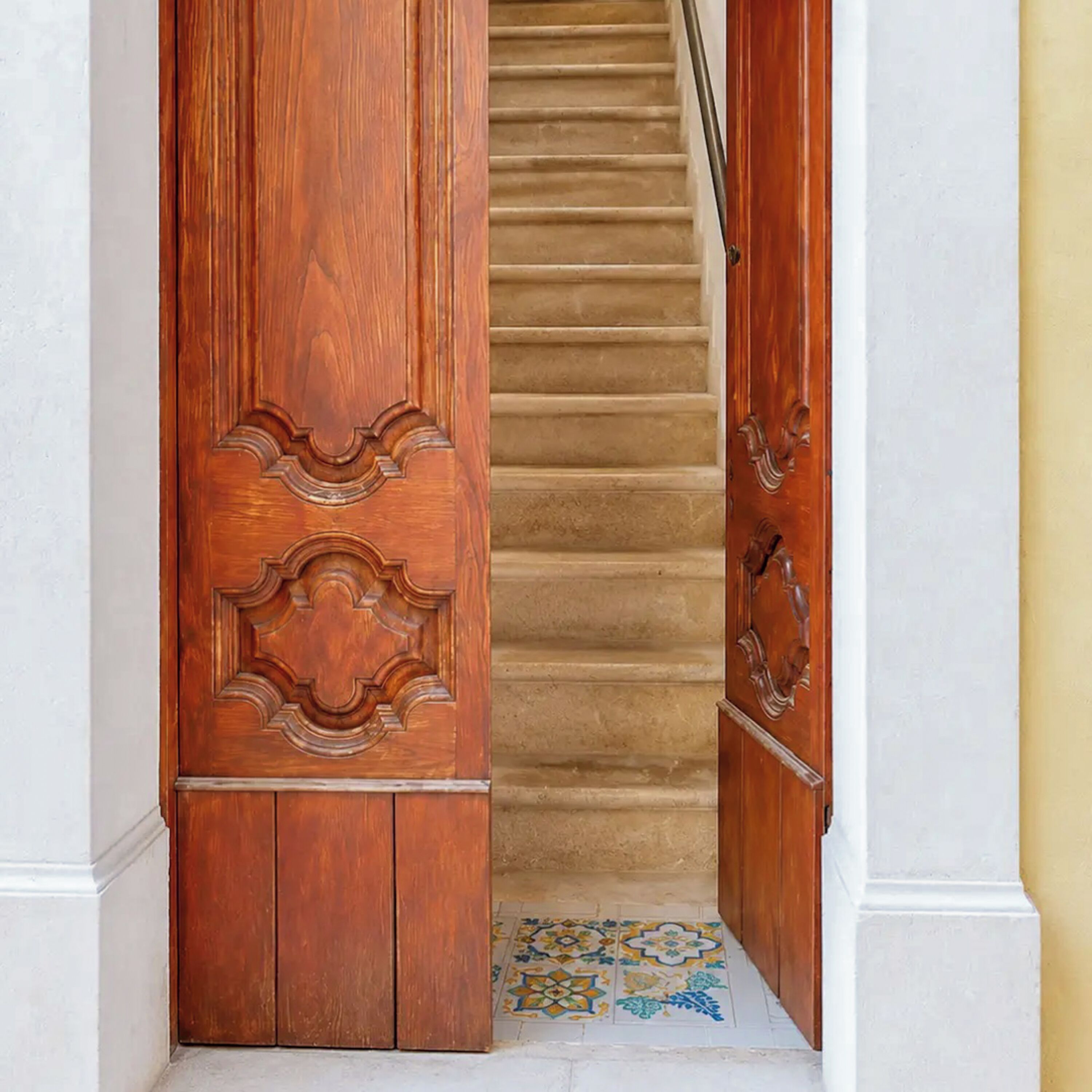 A wooden staircase with a patterned floor leading to a door with intricate carvings.