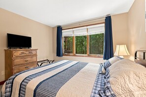 A bedroom with a bed, a dresser, a television, a window with curtains, and a lamp.