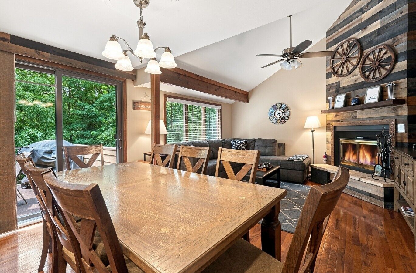 A spacious dining area with a wooden table and chairs, a ceiling fan, and a fireplace with a clock on the wall.