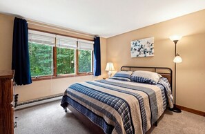 A bedroom with a bed, a window with curtains, a lamp, and a painting on the wall.