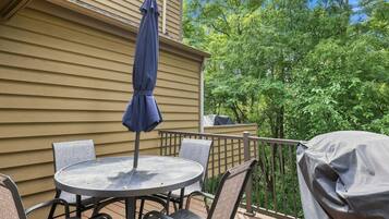 Une table ronde entourée de chaises et surmontée d’un parasol, le tout installé sur un balcon offrant une vue sur les arbres.