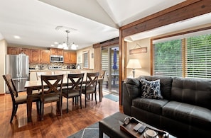 A modern kitchen with wooden cabinets, a stainless steel refrigerator, and a dining area with a table and chairs.