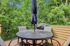 A round table with four chairs and a single umbrella on an outdoor deck.
