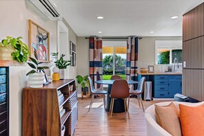 Una cocina moderna con armarios azules, una zona de comedor con mesa y sillas, y una sala de estar con sofá y televisor.