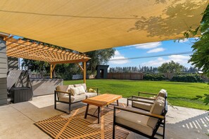 Un patio exterior con una pérgola de madera, un sofá, una mesa y sillas.