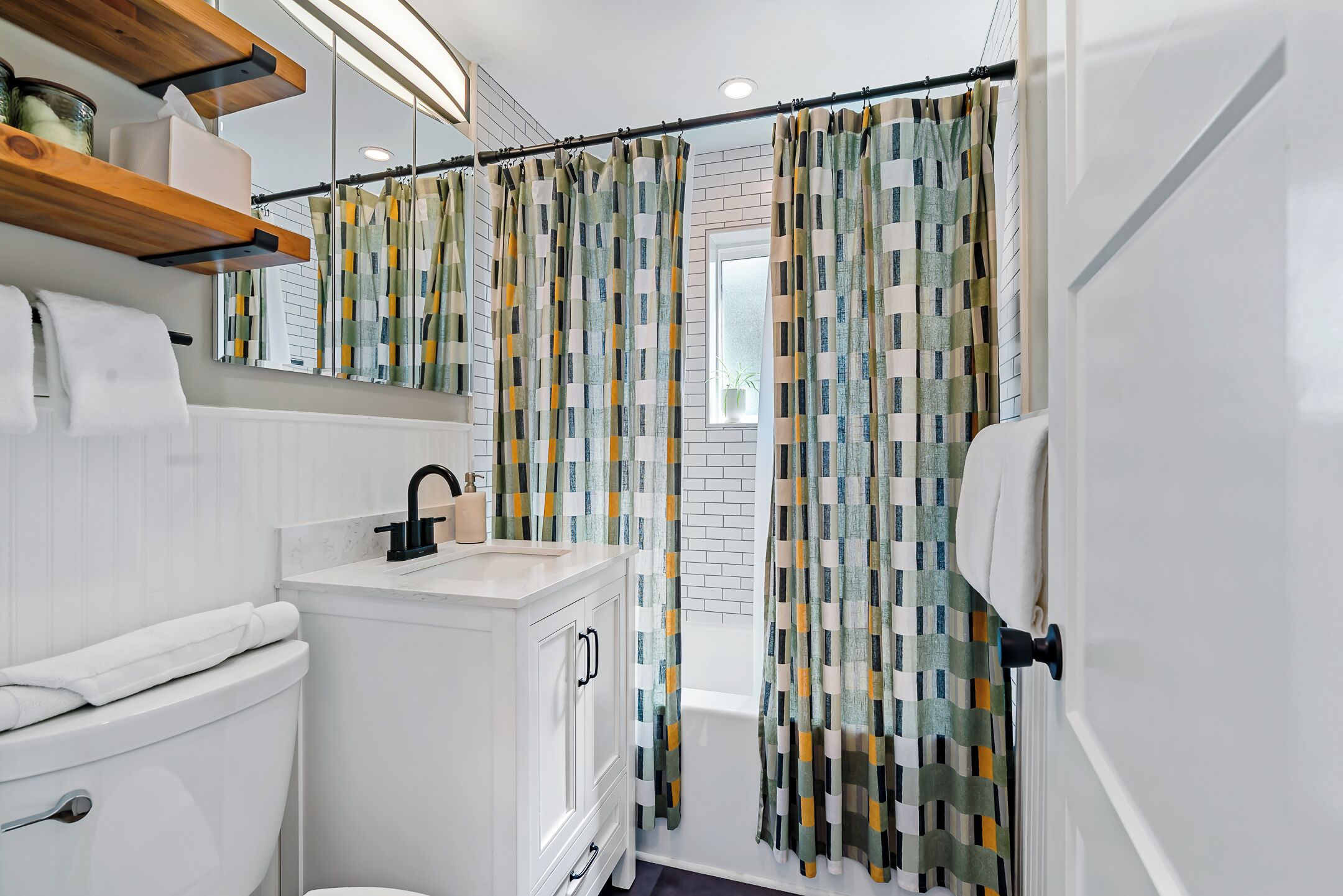 A modern bathroom with a white sink, toilet, and vanity. There is a shower curtain with a geometric pattern.
