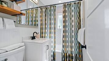 A modern bathroom with a white sink, toilet, and vanity. There is a shower curtain with a geometric pattern.