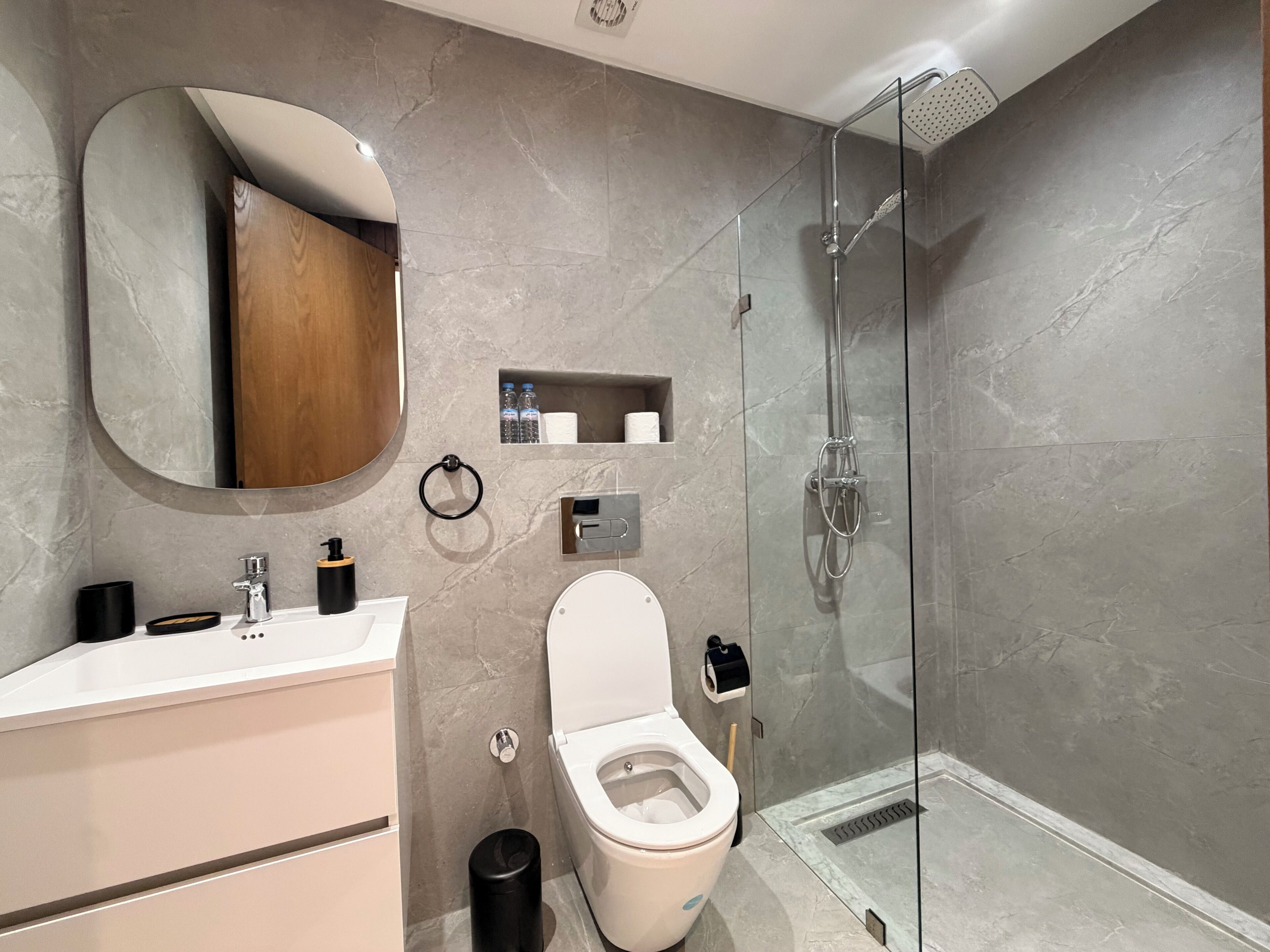A modern bathroom with a toilet, sink, mirror, and shower.