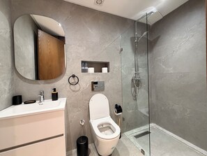 Un baño moderno con inodoro, lavamanos, espejo y ducha.