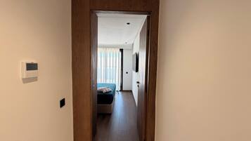 Un pasillo que conduce a un dormitorio con una cama, un termostato en la pared y una puerta con marco de madera.