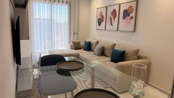 A modern living room with a sofa, a glass coffee table, and a flat-screen TV.