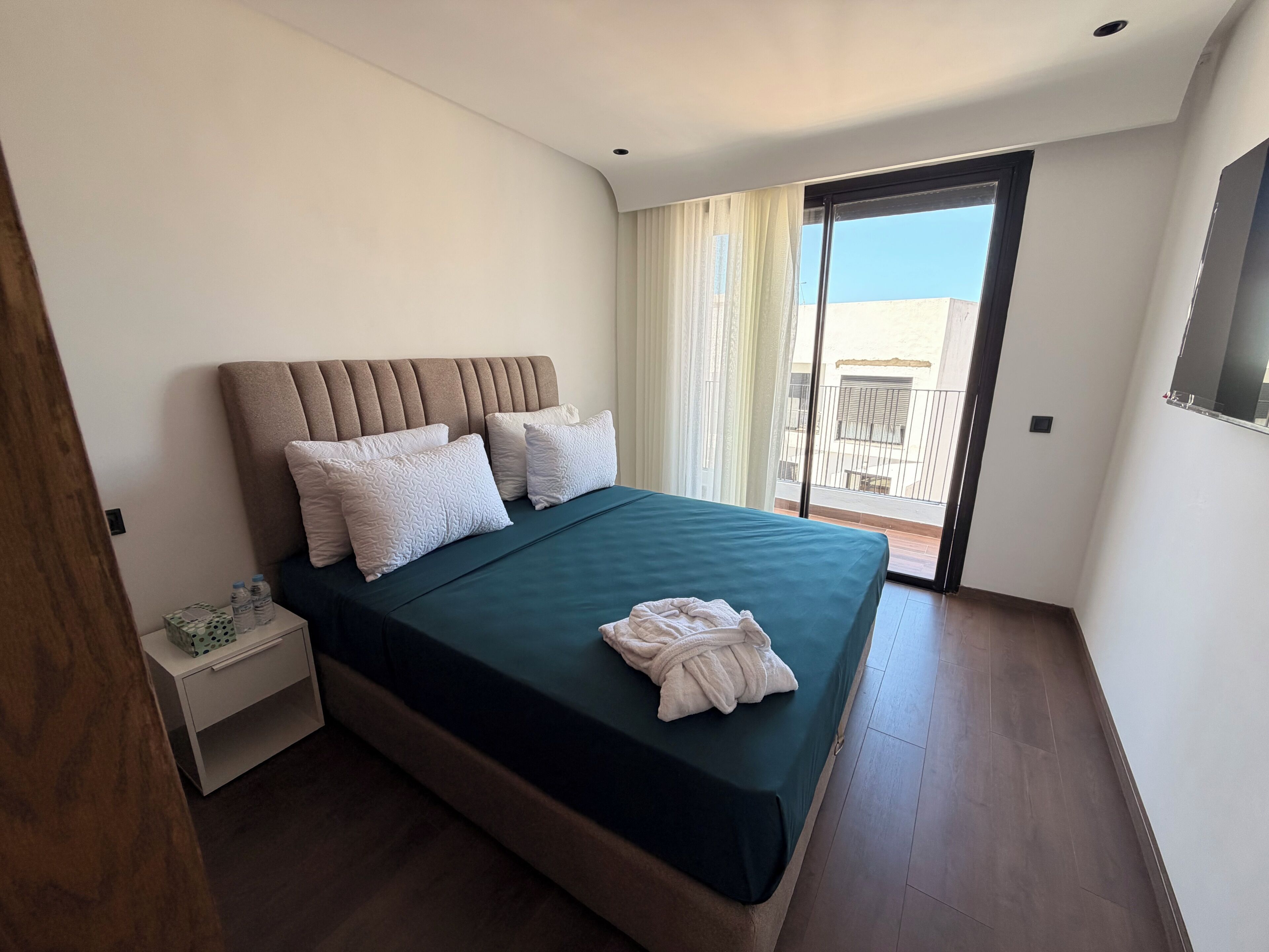 Ein Hotelzimmer mit Bett, Nachttisch, Bademantel und Blick ins Freie.
