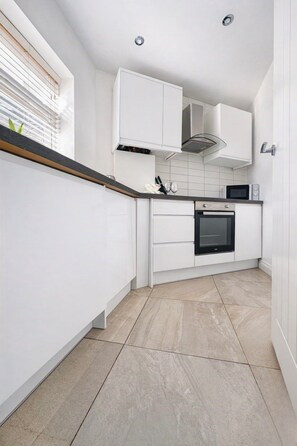 Cocina moderna con armarios blancos, horno integrado y microondas.