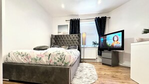 Un dormitorio con cama, televisor, cómoda y ventana con cortinas.