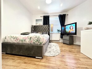 Un dormitorio con cama, televisor, cómoda y ventana con cortinas.