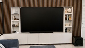 Una sala de estar moderna con una televisión de pantalla plana grande, estantes empotrados, un sofá y un altavoz.