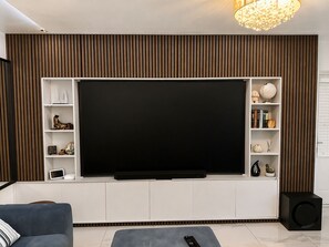Una sala de estar moderna con una televisión de pantalla plana grande, estantes empotrados, un sofá y un altavoz.