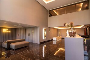 A modern lobby with a reception desk, seating area, and a large vase with flowers. - Mardisa Design Cabo Branco  (João Pessoa)