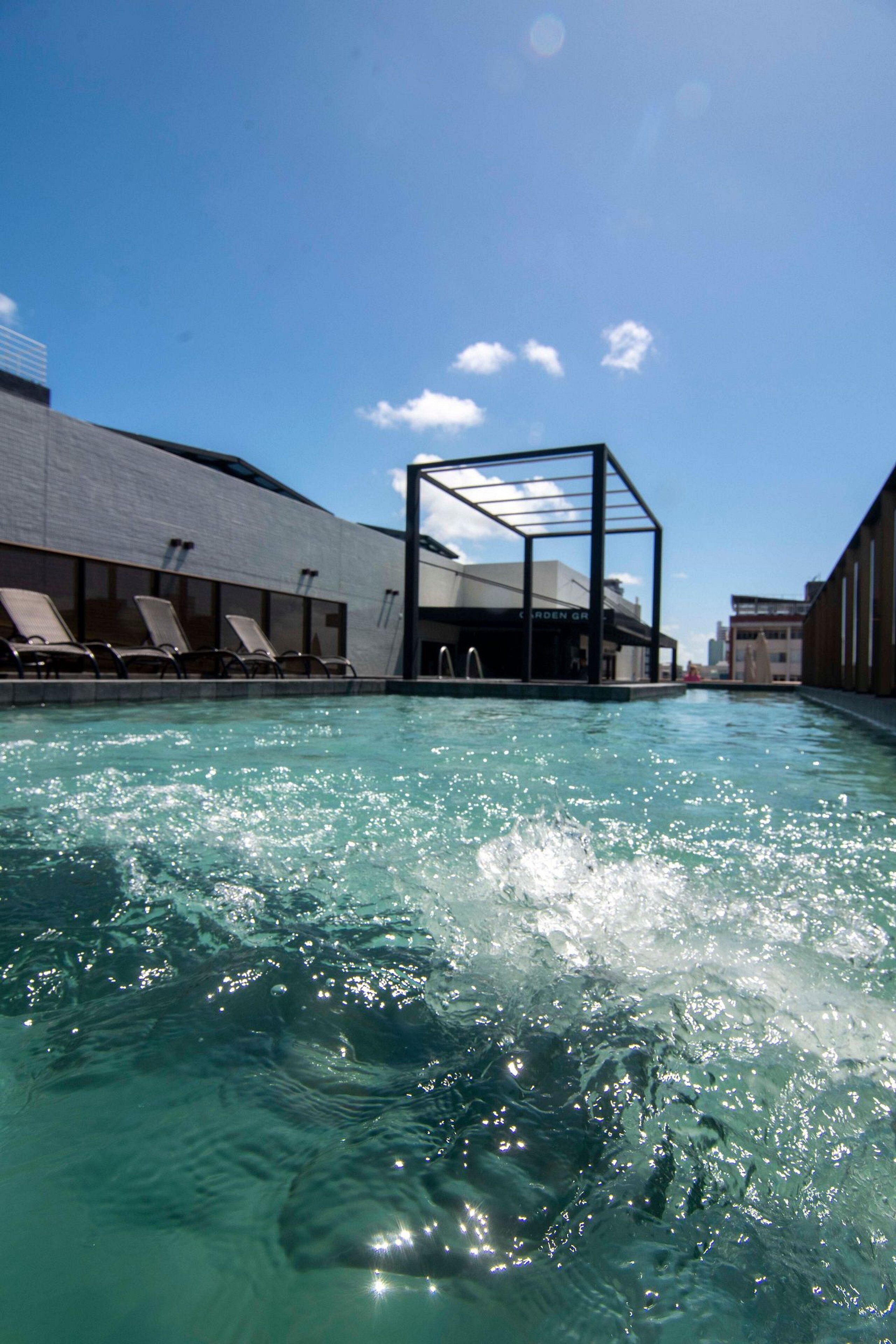 Ein Swimmingpool mit klarem Wasser, ein überdachter Sitzbereich und ein Gebäude mit der Aufschrift 'GARDEN GR'.