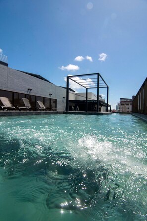 Ein Swimmingpool mit klarem Wasser, ein überdachter Sitzbereich und ein Gebäude mit der Aufschrift 'GARDEN GR'.