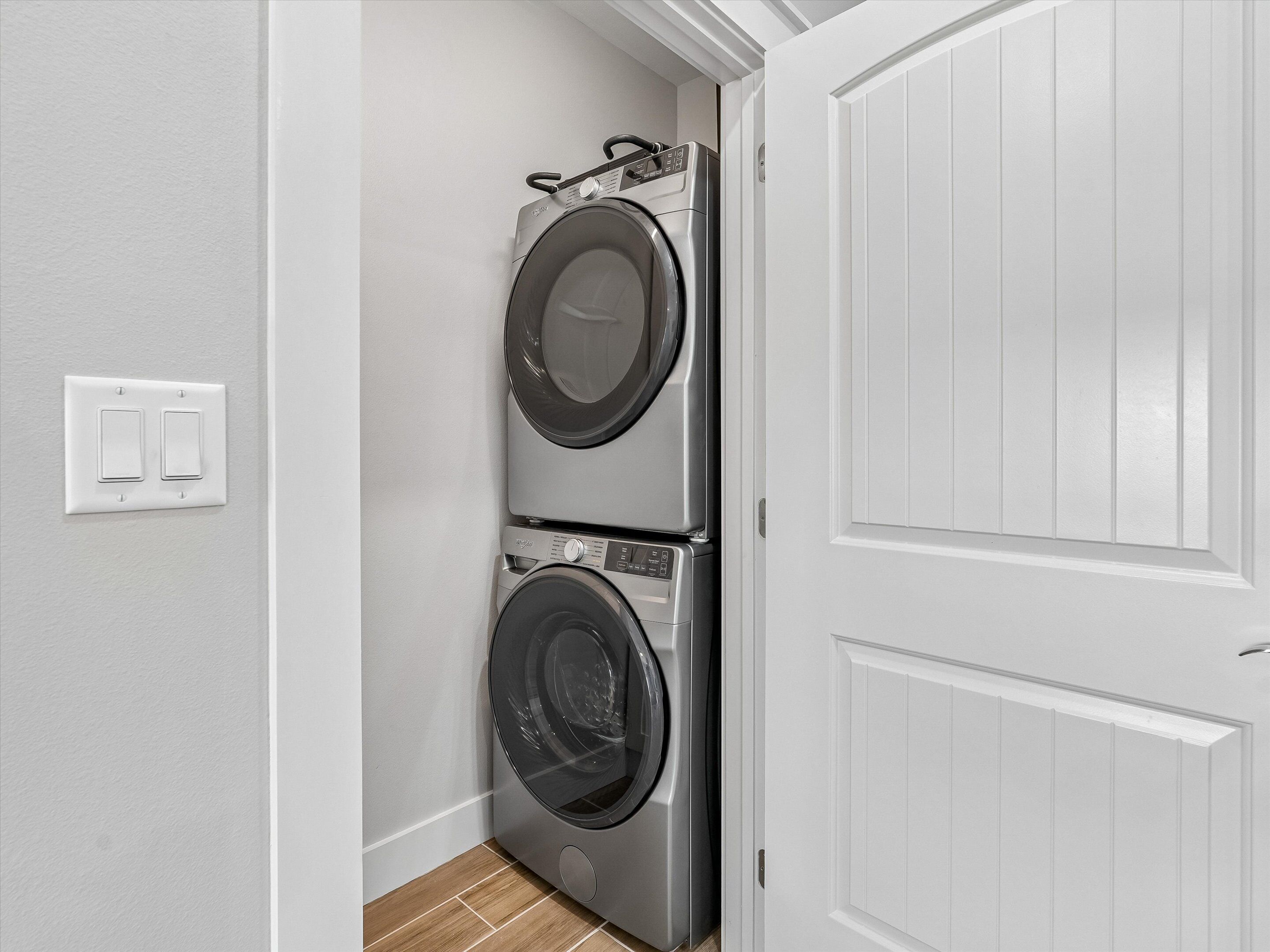 A laundry room with two stacked front-loading washing machines, a white door, and a light switch on the wall.