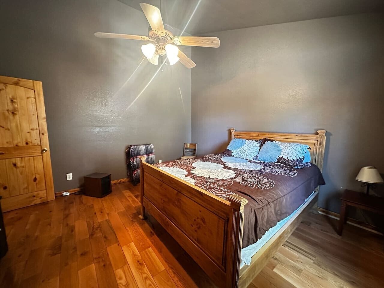 Une chambre à coucher avec un lit en bois, un ventilateur de plafond, une armoire en bois et une petite table de chevet.