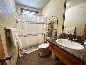 Une salle de bain avec un rideau de douche, des toilettes, un lavabo avec un miroir et des serviettes sur un porte-serviettes.