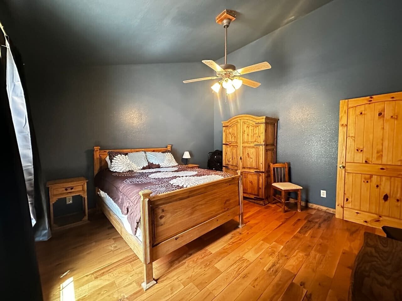 Un dormitorio con una cama de madera, un ventilador de techo, un armario y una mesita.