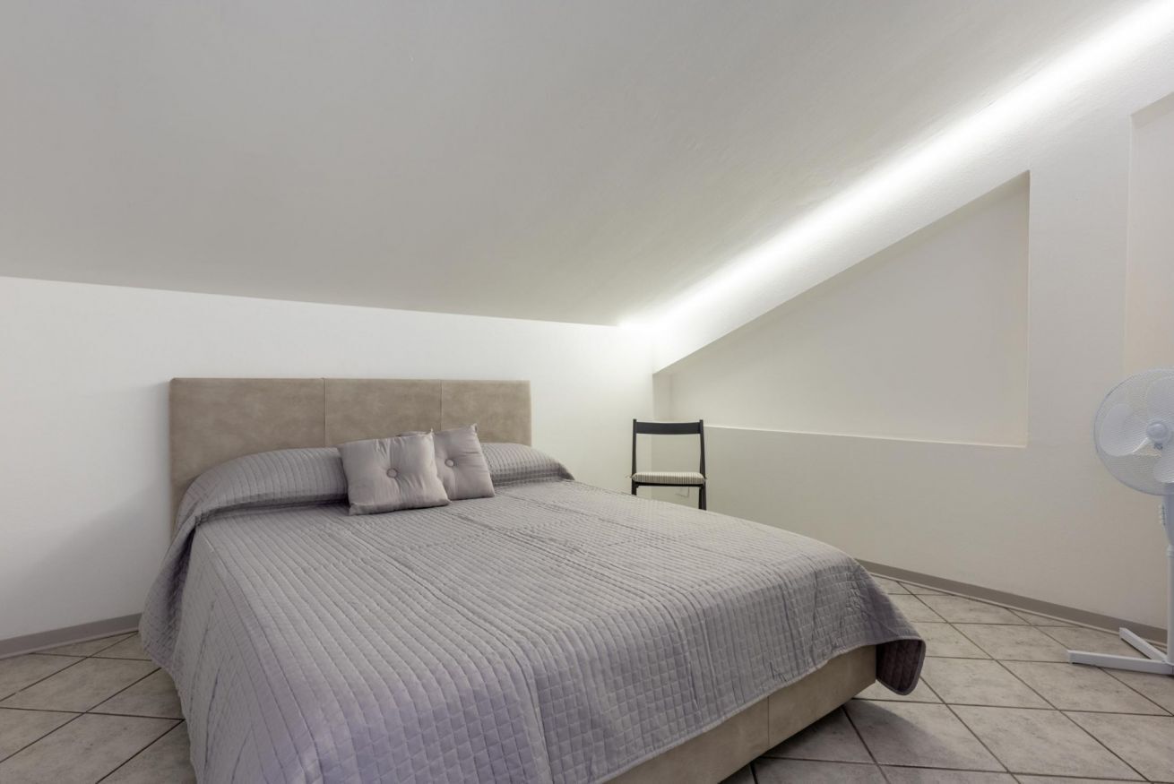 Un dormitorio con cama, una silla y un ventilador de pie.