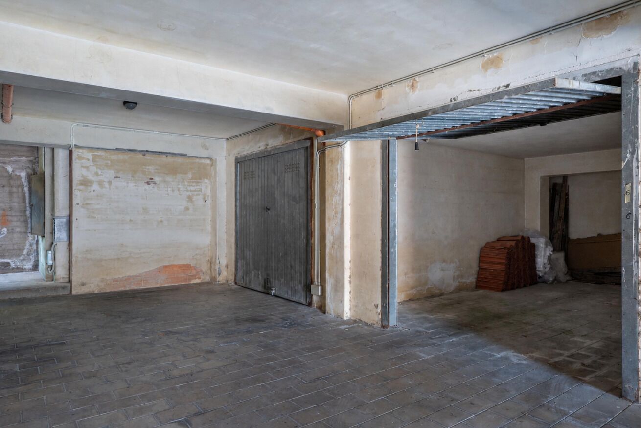 Una habitación con una puerta cerrada, estructura de viga metálica y suelo de ladrillo.