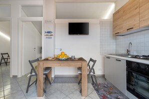 A modern kitchen with a dining table, chairs, a TV mounted above the counter, and a tiled backsplash. - GuestHost - BaiAmare - Attic with Pool & Parking (Capo Mulini)