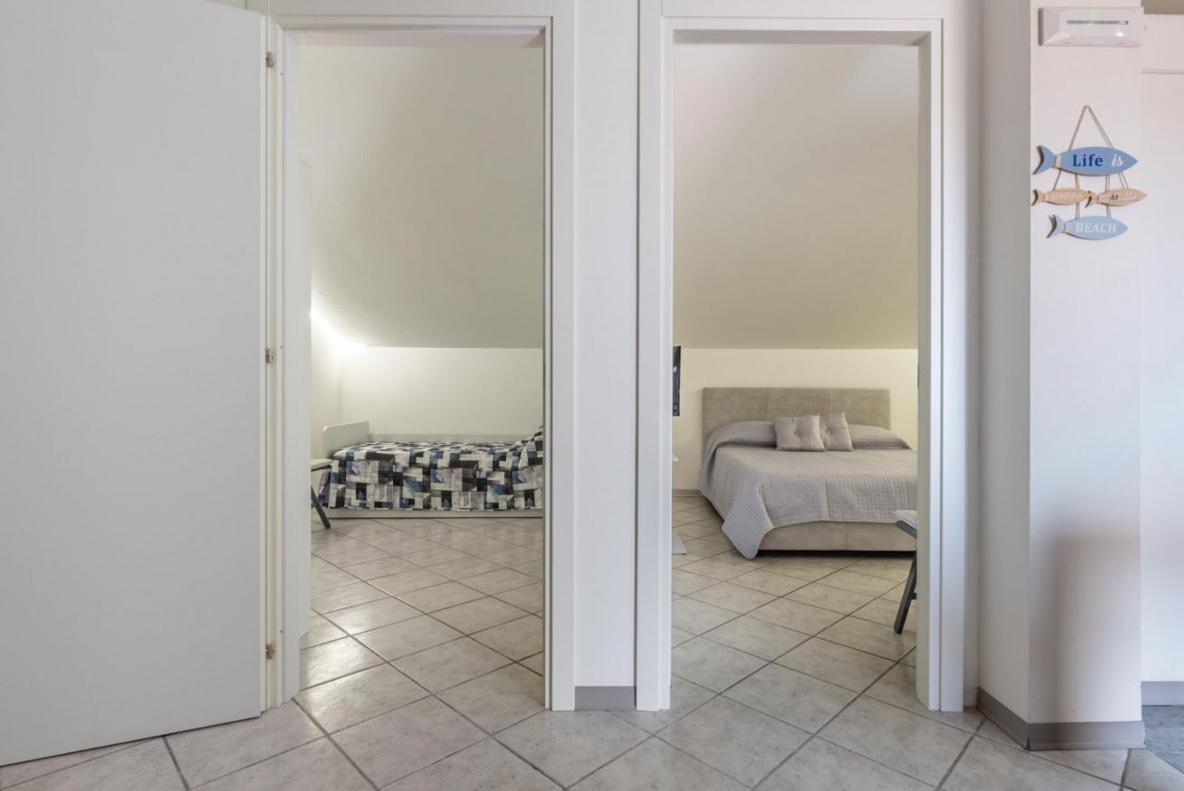 Habitació amb un llit, una cadira i una taula. Hi ha una porta que condueix a una altra habitació.