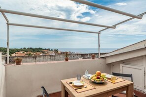 A balcony with a table set for dining, overlooking a coastal town. - GuestHost - BaiAmare - Attic with Pool & Parking (Capo Mulini)
