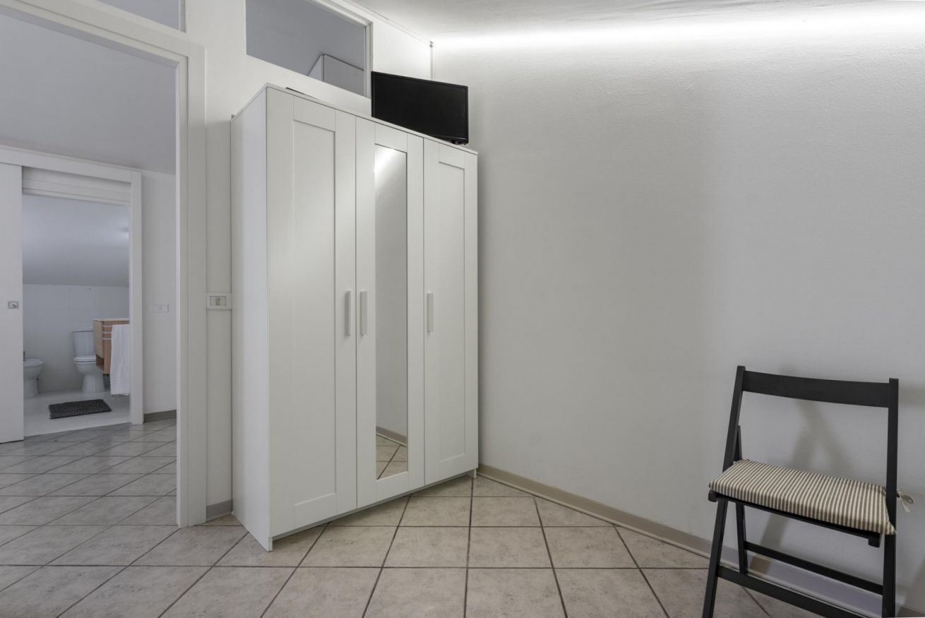 A room with a white wardrobe, a chair, and a television on top of the wardrobe.