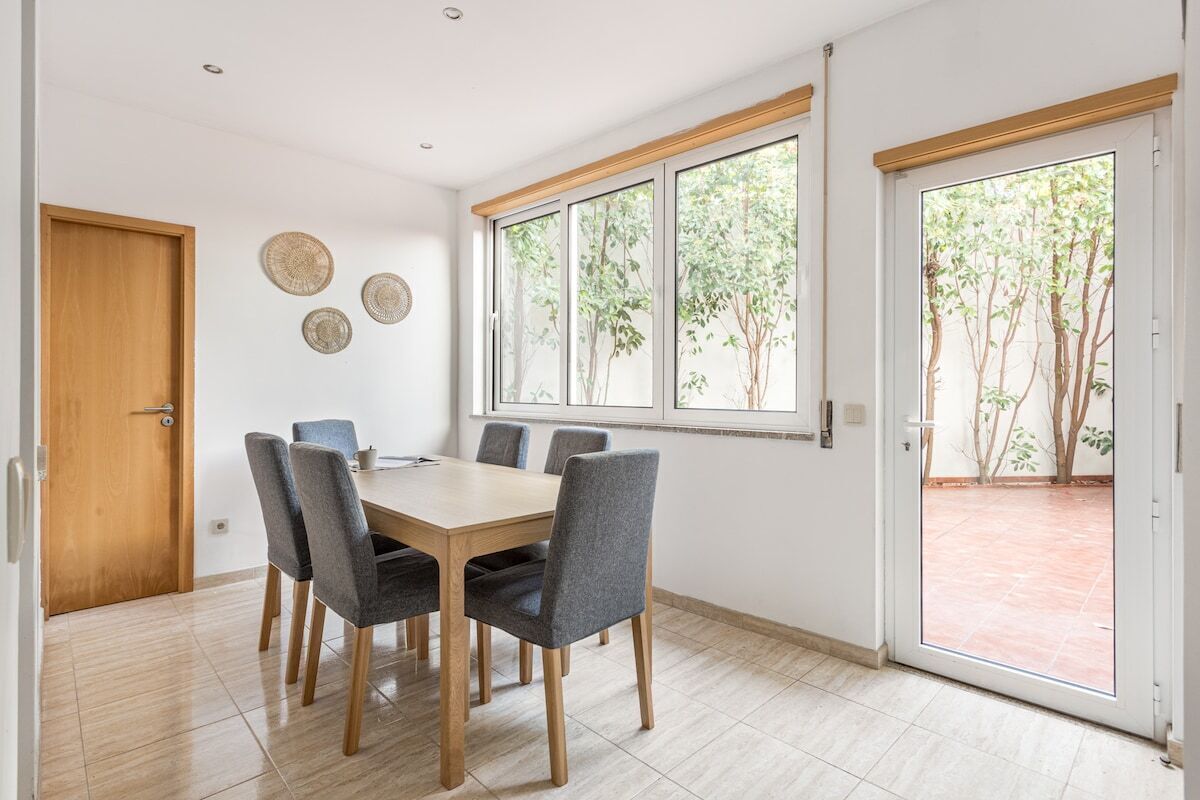 A dining area with a wooden table and grey chairs, a wooden door, and a window with a view of trees.
