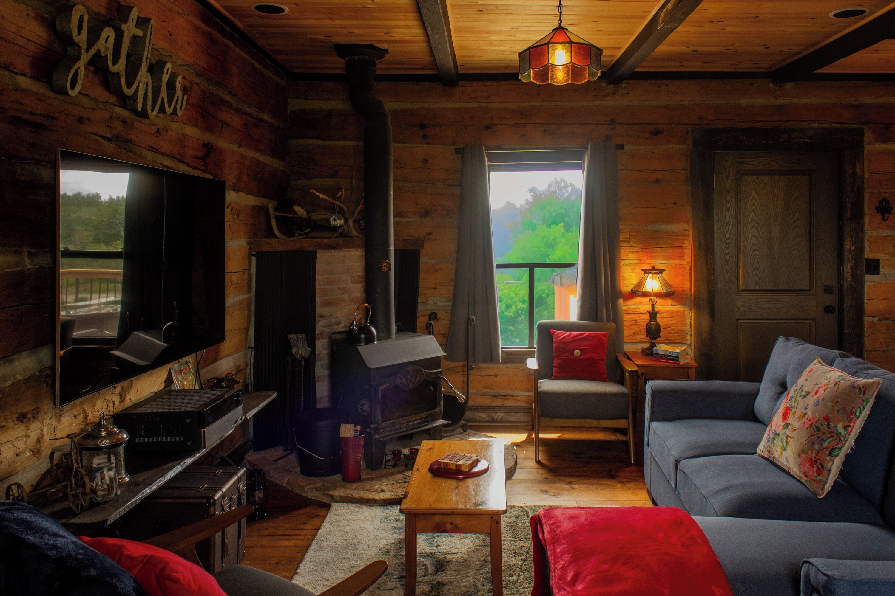 A log cabin interior with a fireplace, sofa, television, and a view of the outdoors.