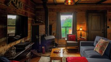 Een chaletinterieur met een open haard, bank, televisie en uitzicht op het omliggende landschap.
