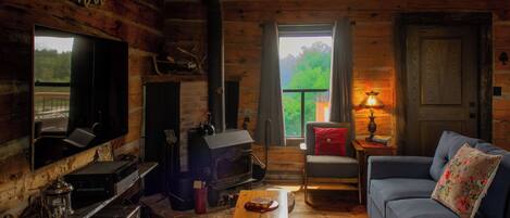 A log cabin interior with a fireplace, sofa, television, and a view of the outdoors.
