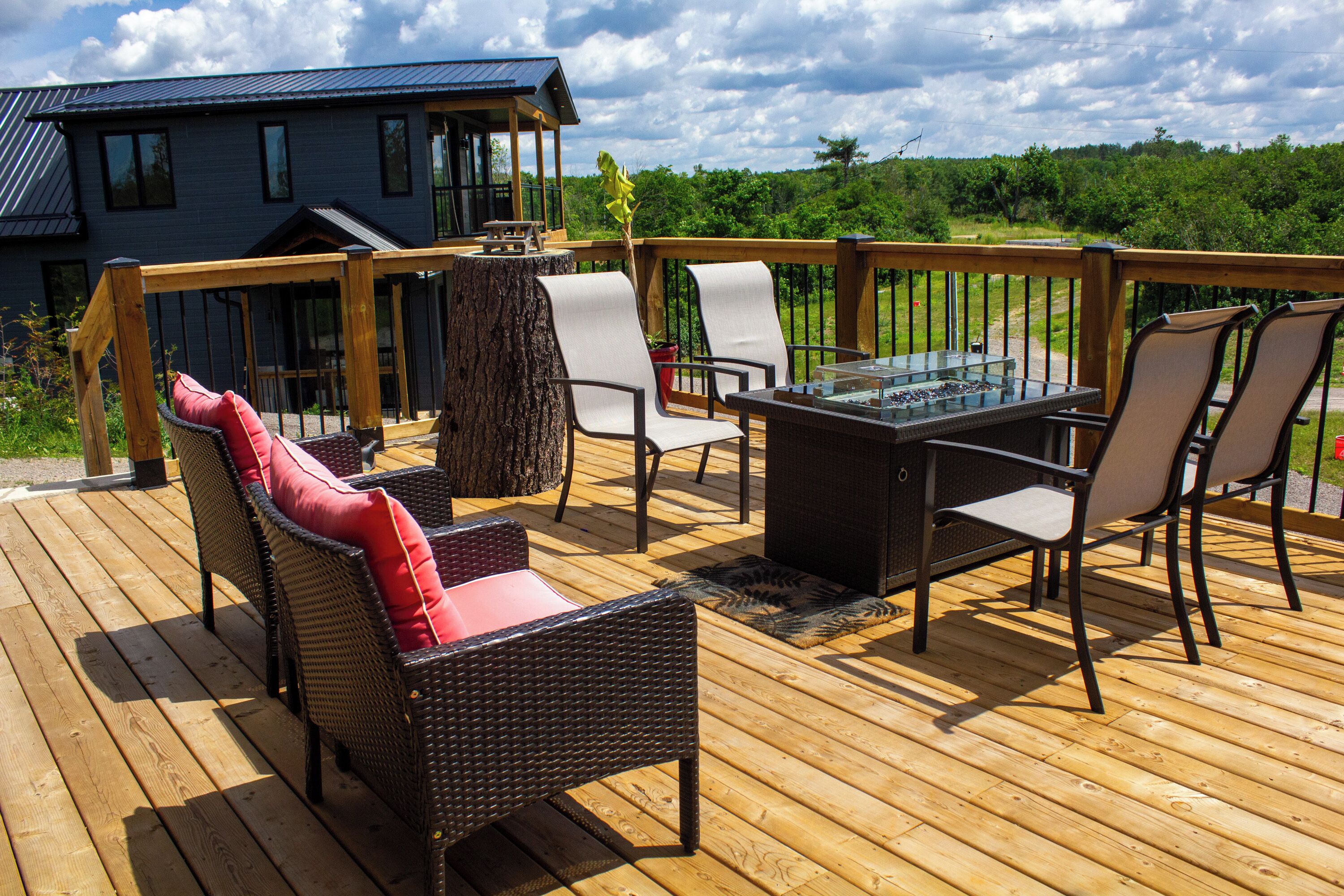 A wooden deck with outdoor furniture, including a table and chairs, overlooking a house and greenery.