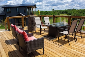 A wooden deck with outdoor furniture, including a table and chairs, overlooking a house and greenery. - The Lodge | Historic Log Cabin + Hot Tub + Beach Access (Tweed)